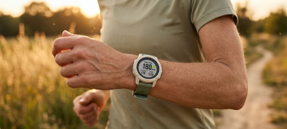 Coureuse vérifiant sa montre cardio affichant 180 bpm pendant un footing en pleine nature au lever du soleil