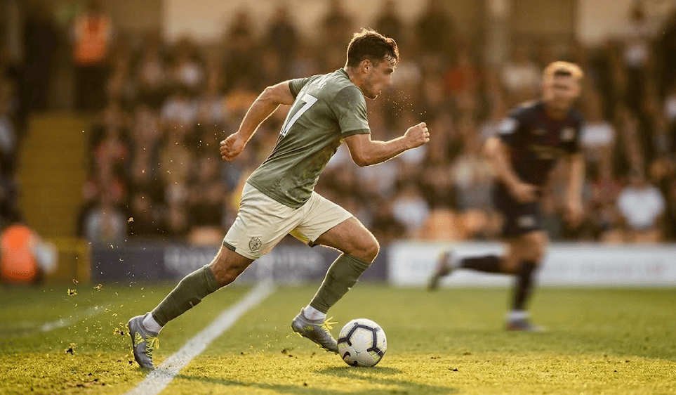 Ailier de football lancé à pleine vitesse en contre-attaque, lumière dorée de fin de match
