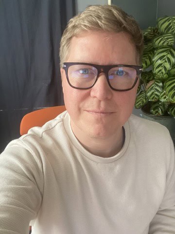 Julien Rommelard, auteur de Positive Nation : portrait en intérieur, lunettes à monture noire et pull écru